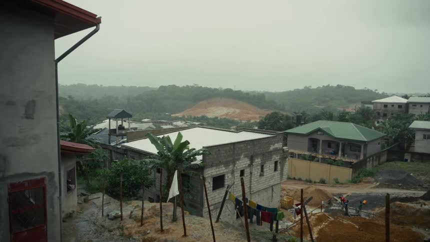 Houses under construction surrounded by hills and vegetation under cloudy weather