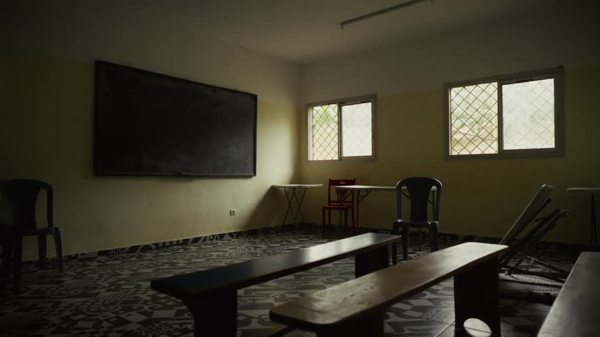 Blackboard hangs on the wall of an empty school room being used to store furniture during the daytime