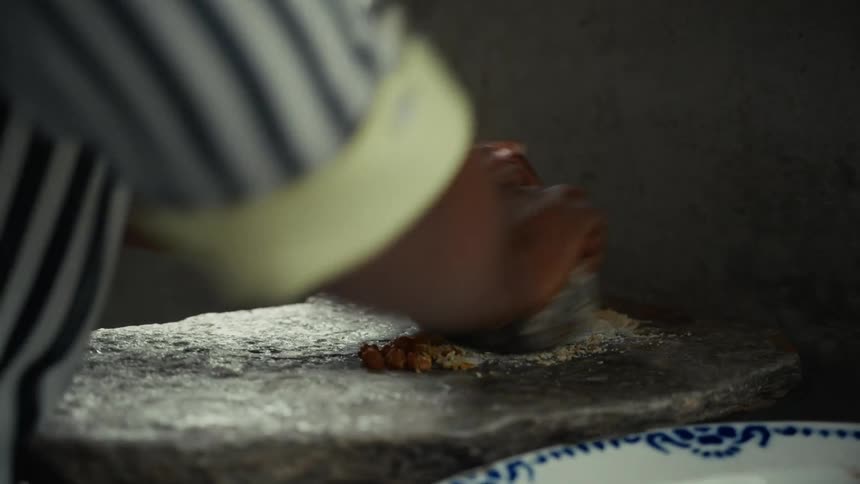 A person is using a rock and a slab to grind some food into powder