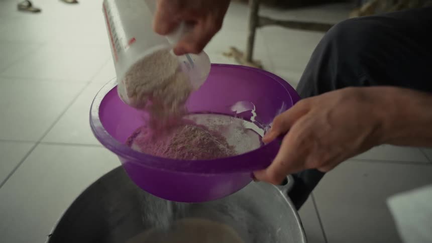The man pours flour through a strainer into a bucket