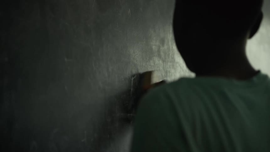 Youth cleans off the blackboard with an eraser during the daytime