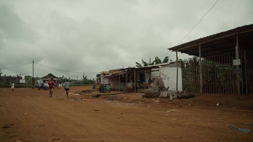 Dirt road with small buildings and people walking under a cloudy sky
