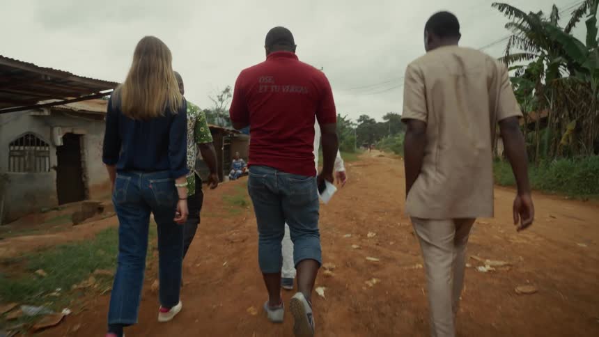 A group of people is walking down a dirt road in a remote village
