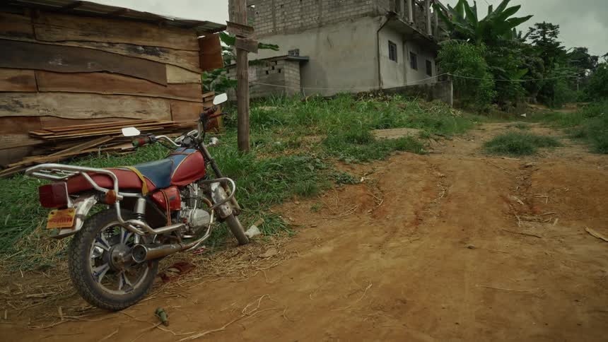 Motorcycle parked on a rural dirt road near dilapidated buildings