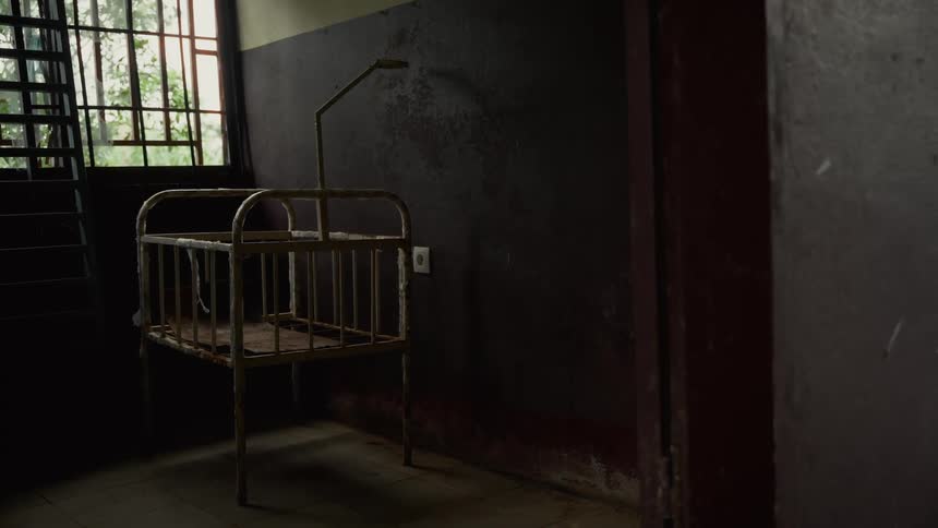 Old worn crib stands in a room near the window on a summer day