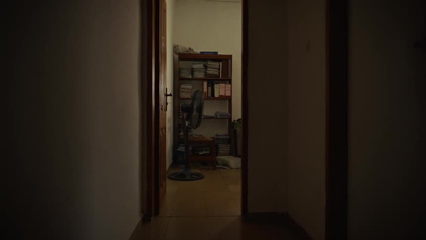 A standing fan and a bookshelf positioned in a room from a corridor indoors during daytime
