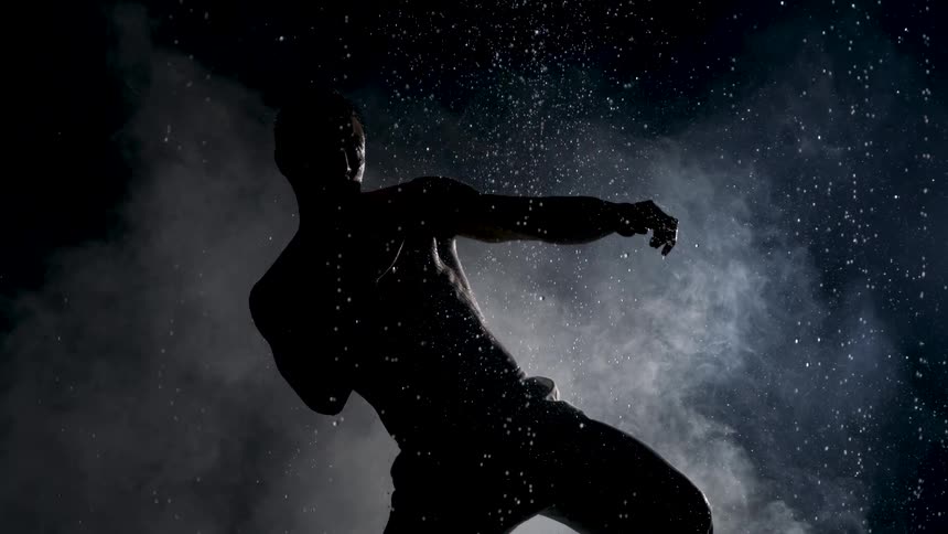 Silhouetted person kicks amid a burst of powder against a dark background