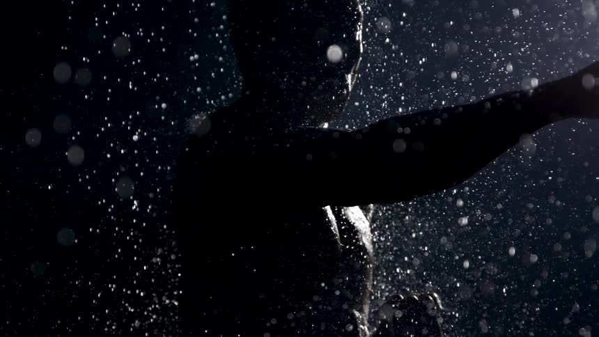 A man is shadow boxing outdoors at night while it rains