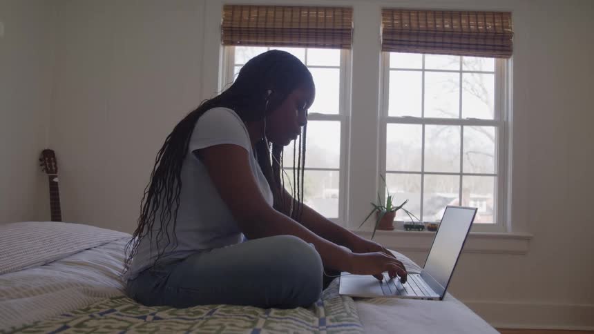Woman sitting on her bed typing on a laptop computer