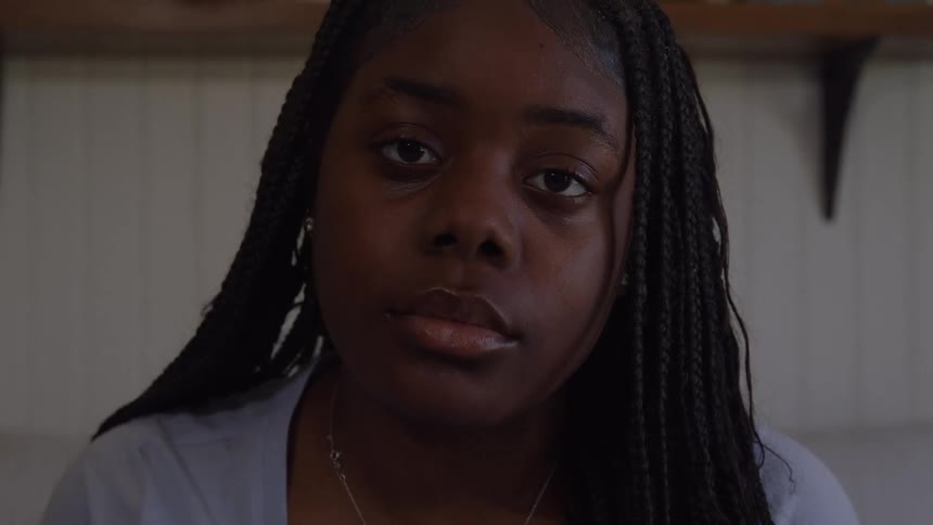 A teenage girl looks down in thought inside a softly lit room