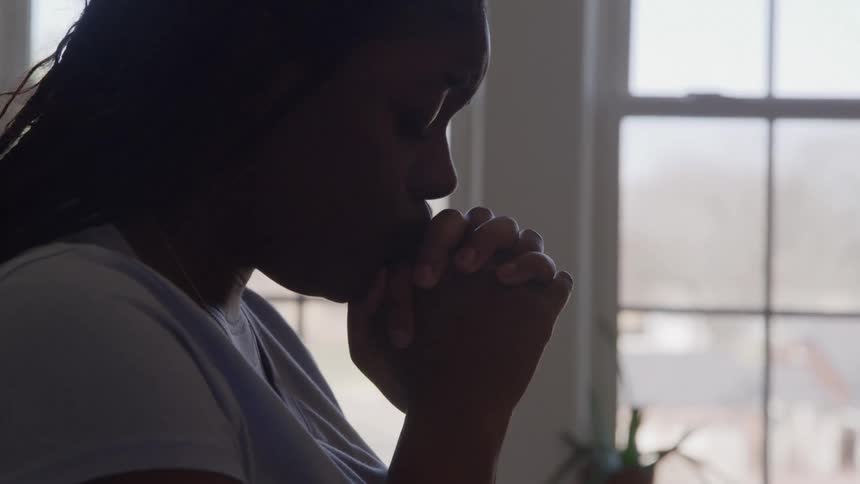 Woman prays silently with hands clasped before the window