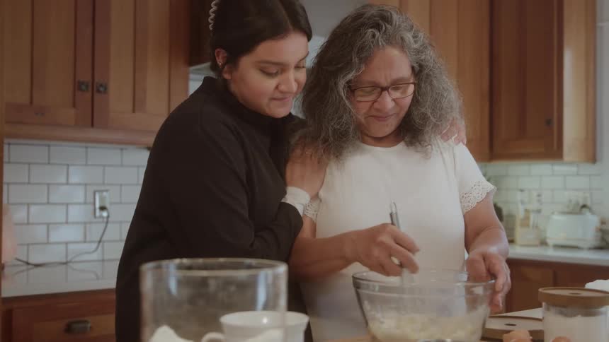 An older woman mixing ingredients in a glass bowl while being hugged