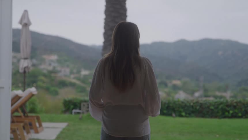 A woman is standing in her yard looking out over a rural mountain town