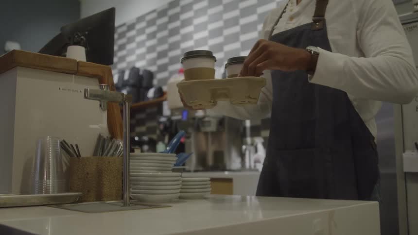 A male server at a cafe counter hands a woman her drinks