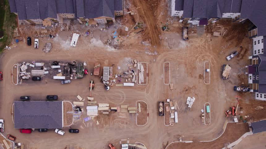 Several vehicles are parked in a dirt lot at a building construction site