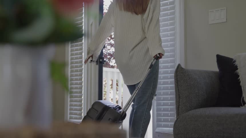Woman leaves the house pulling a suitcase