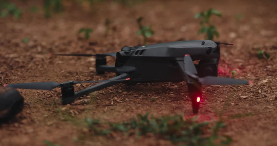 Male hand placing a black drone with flashing lights on the ground outdoors during day time