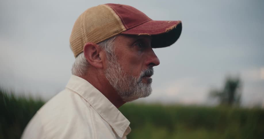Man adjusts his cap while gazing at the field in the distance
