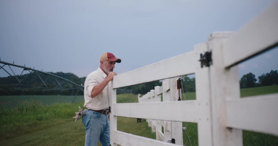 Man opens the gate of a white fence in a rural area