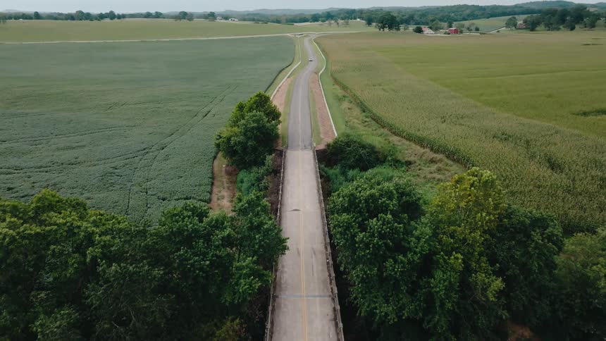 A car driving toward a bridge on a lonely countryside road at midday