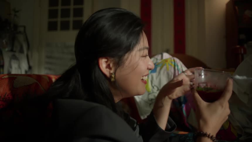 Two teenage female friends sharing a drink while sitting on the couch in the living room
