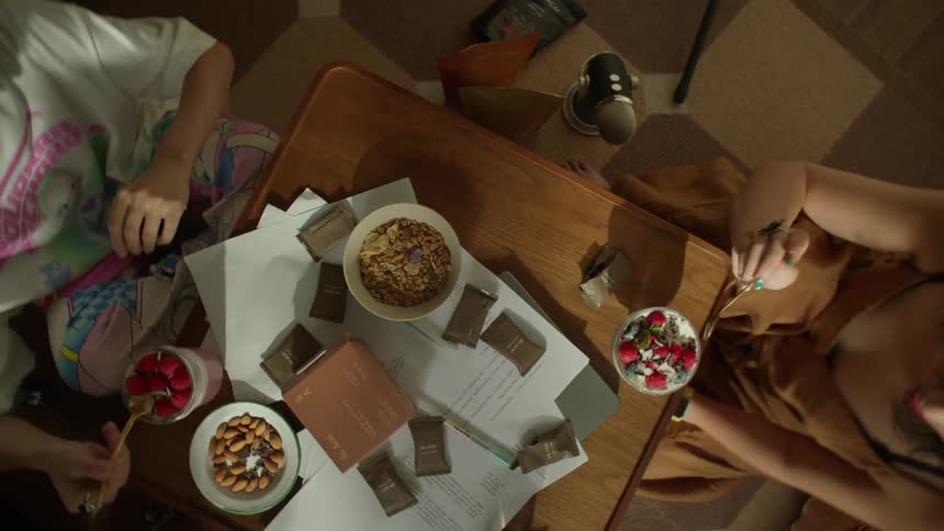 A top view of a group of friends sharing a meal of berries granola and almonds while papers and small packages are scattered on a wooden coffee table