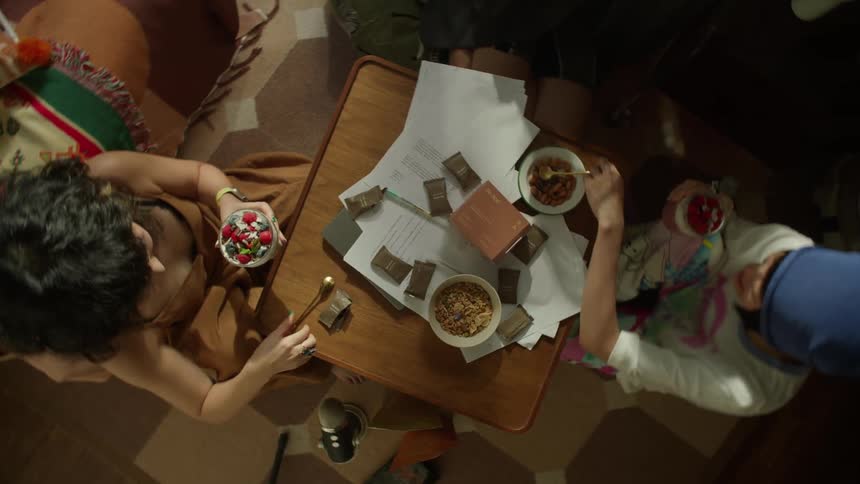 A group of friends sits on the floor enjoying a casual snack of fruit and granola around a coffee table