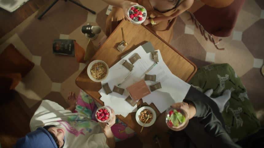 Friends sitting on the floor make a toast with their healthy fruit and granola snacks over a coffee table