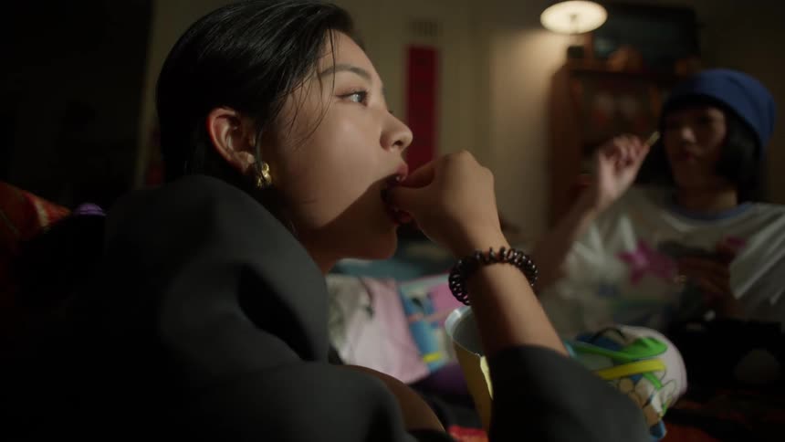 Two young women are relaxing and eating snacks together in a cozy dimly lit room
