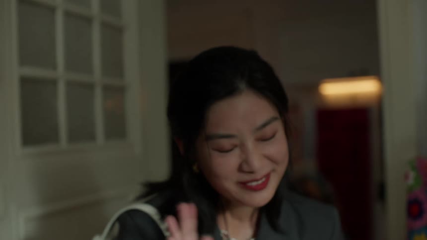 A smiling woman waves her hand while walking into the room