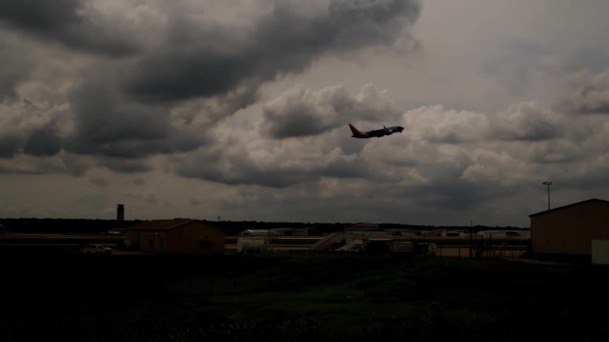 An airplane ascends into a dark dramatic sky filled with heavy storm clouds climbing above the silhouetted airport grounds below