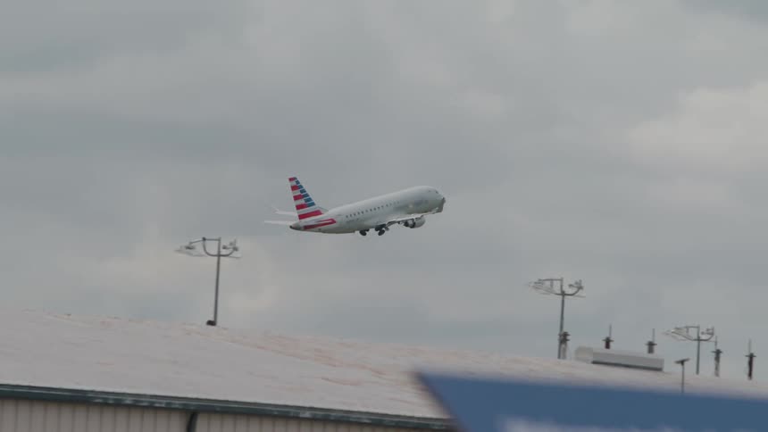 Airplane takes off under a cloudy sky with airport structures in the background