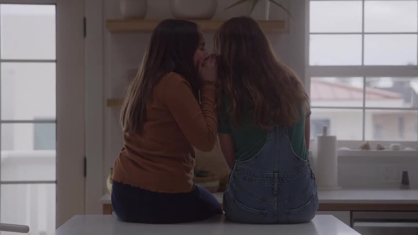 Girls sitting on the counter share a whispered secret