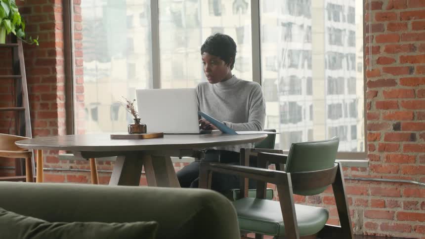 Woman works on a laptop while sitting near a window during the day