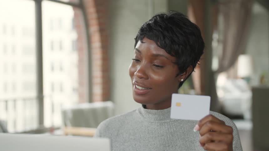 Woman sitting at a table with a laptop computer as she holds up a card and smiles
