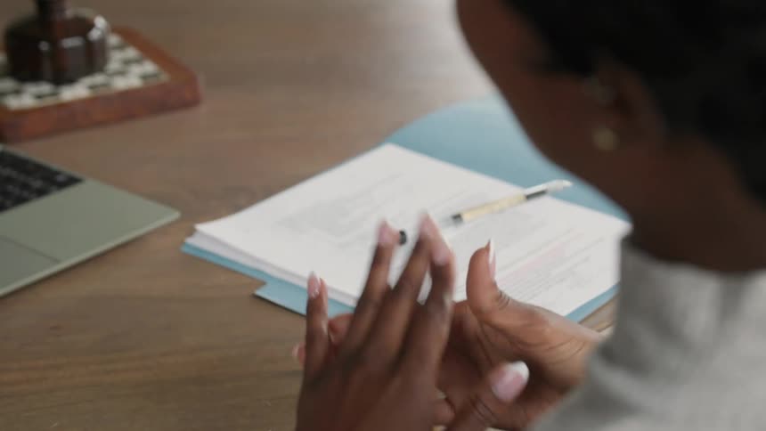 Woman gestures with her hands while talking beside a table with documents
