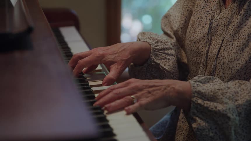A person is in a room seated at a wooden piano playing the piano