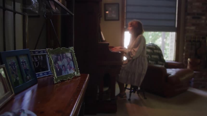 Woman plays the piano in the background while framed photos decorate the furniture in the foreground