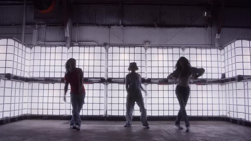 Three dancers perform a dance routine near a brightly lit wall