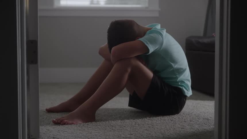Boy sitting on the floor in a room with his head down