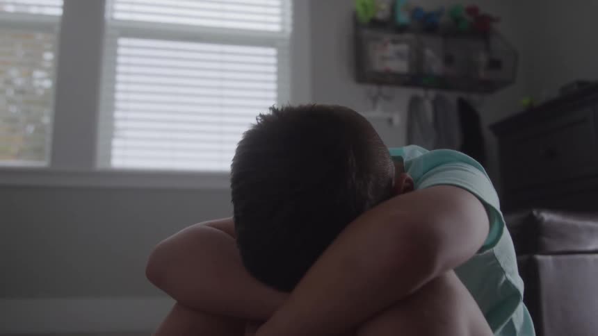 Boy sits on the floor with his head resting on his arms crossed over his knees