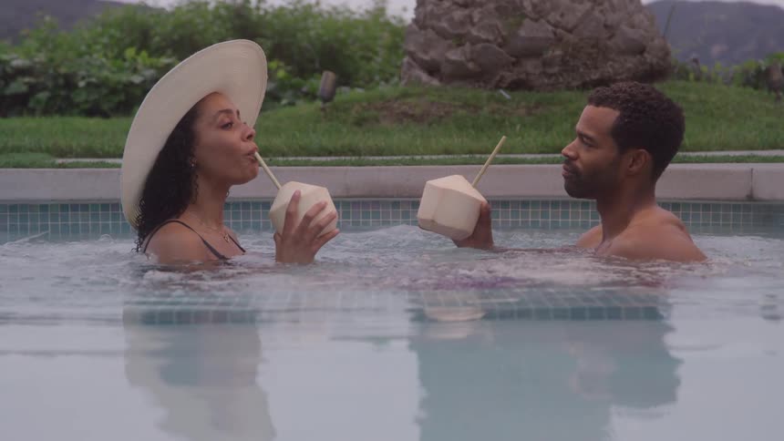 A man and a woman are in a pool that is making bubbles and they are drinking from a cup with a straw