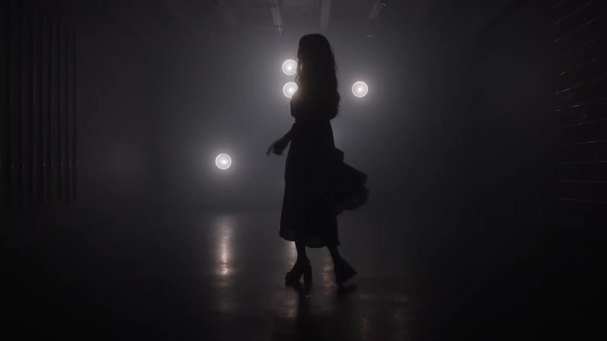 Silhouette dances in a dim space lit by lights in the background