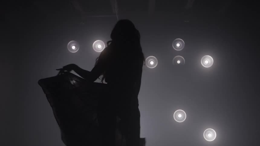 Silhouette poses with a hand on the hip in front of bright lights