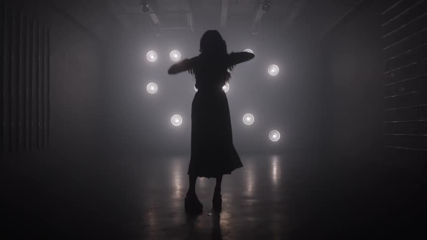 Silhouette dances with raised arms in front of bright lights