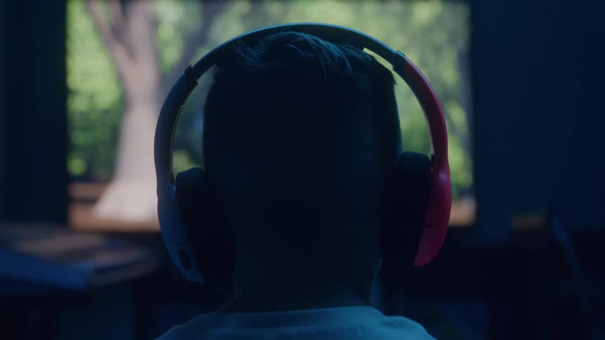 Male gamer wearing headphones plays a computer game in a dimly lit room