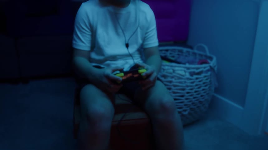 Child plays video games wearing headphones in a room lit by blue light