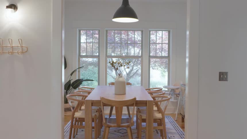 Bright dining room features a wooden table with a central arrangement in front of large windows