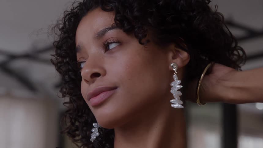 Woman with curly hair wears pearl earrings