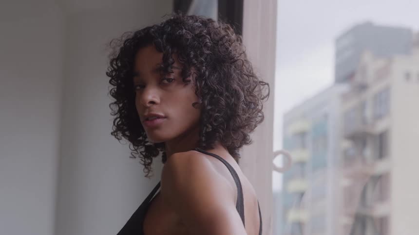 Woman looks back near the window with blurred buildings in the background